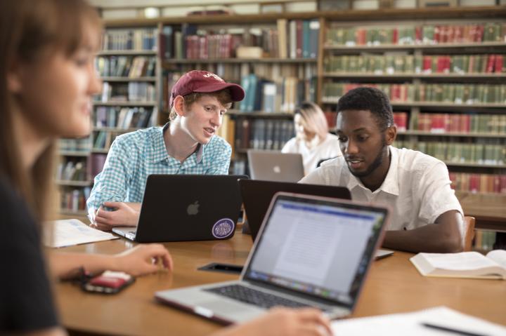 Two students studying in the library with laptops