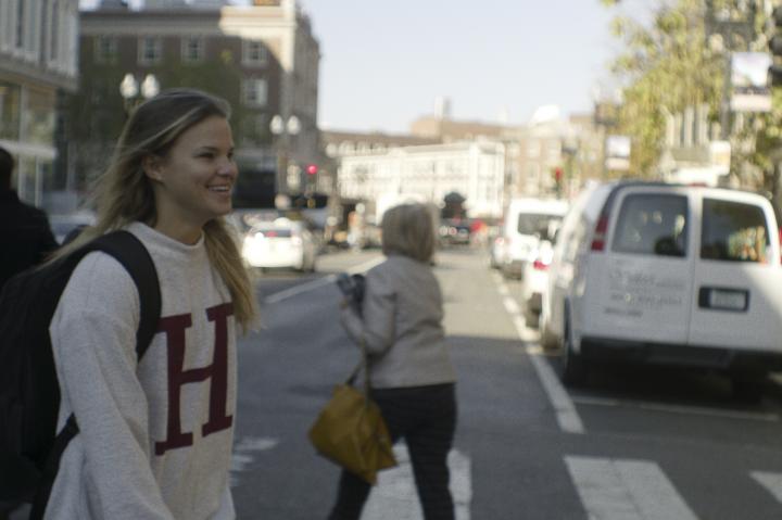 A student wearing an H sweatshirt walking across Harvard Square