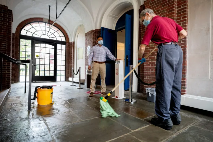Harvard custodial manager Elson Callejas (left), who led the distribution of “cleaning kits” to 1,200 students moving onto campus, is shown in Lowell House with worker James Normile.