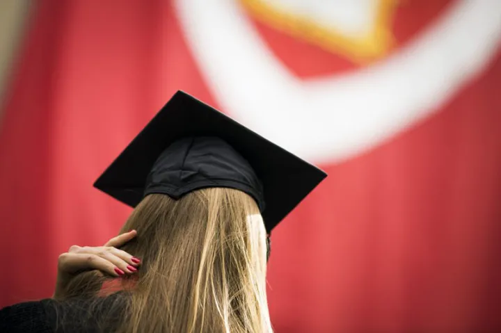 back of a  student's head - shown wearing cap and gown with a banner in the background with the veritas shield