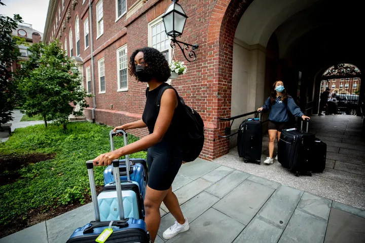 Halima Badri ’23 (left) and Maria Gonzalez ’23 enter the Lowell House courtyard with their luggage.