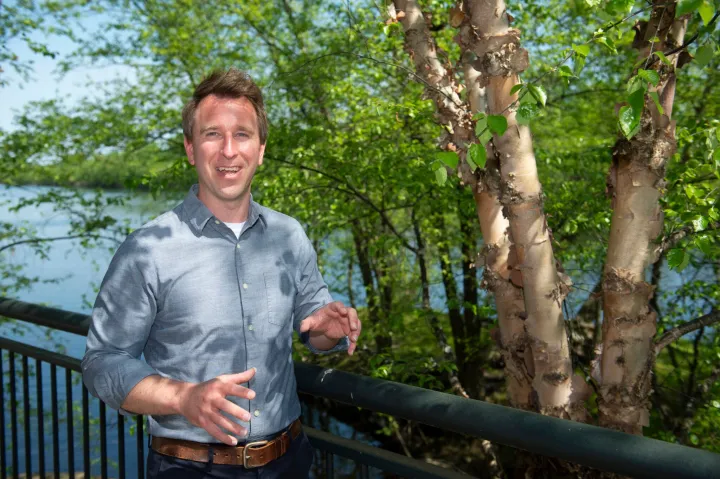 Jeffrey Wilson smiles next to a tree and in front of a water body