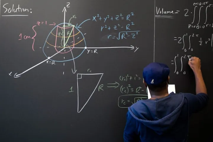 Hakim Walker, preceptor of mathematics, uses the chalkboard in the Science Center math lounge to try to solve a problem: finding the volume of a ball with a 2-centimeter-long cylindrical hole drilled through it.
