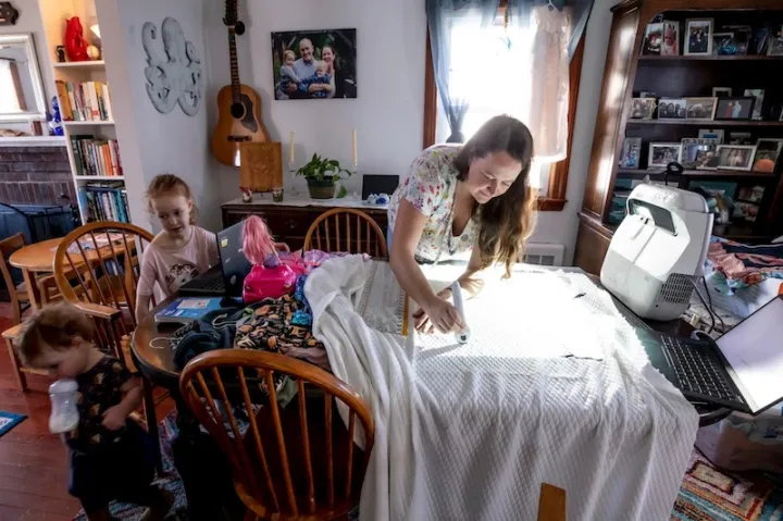 Kate Pease, assistant director of leasing and space planning, sews at home using a projector to draw her pattern. Daughters Ella and Coraline are on left.