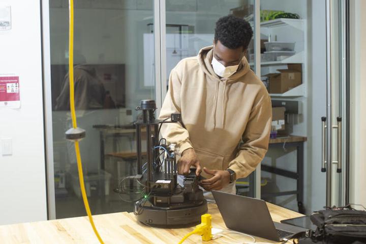 Second-year student Emeka Ezike adjusts his robot during a "CS286: Multi-Robot Systems – Control, Communication, and Security" mini-hack in the Science and Engineering Complex.