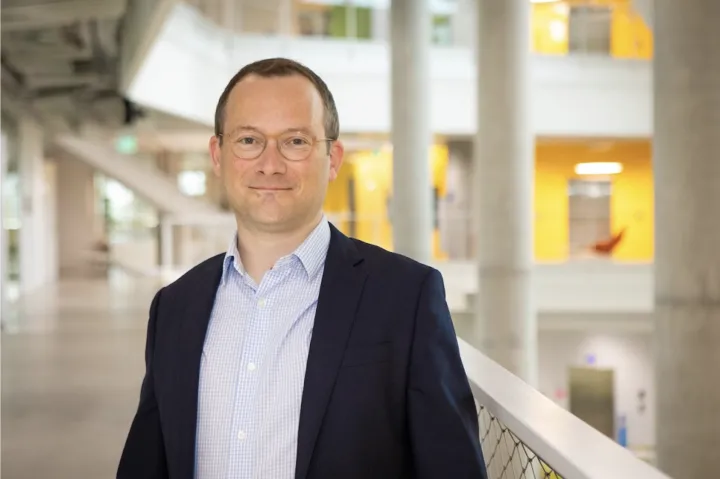 New SEAS Dean David Parkes smiles at the camera with the first floor of the Science and Engineering Complex (SEC) in the background.