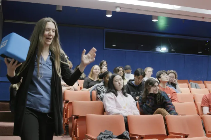 female professor walking around the class  - The classroom has stadium-type seating, and the professor is holding a blue cube that says "catch box".