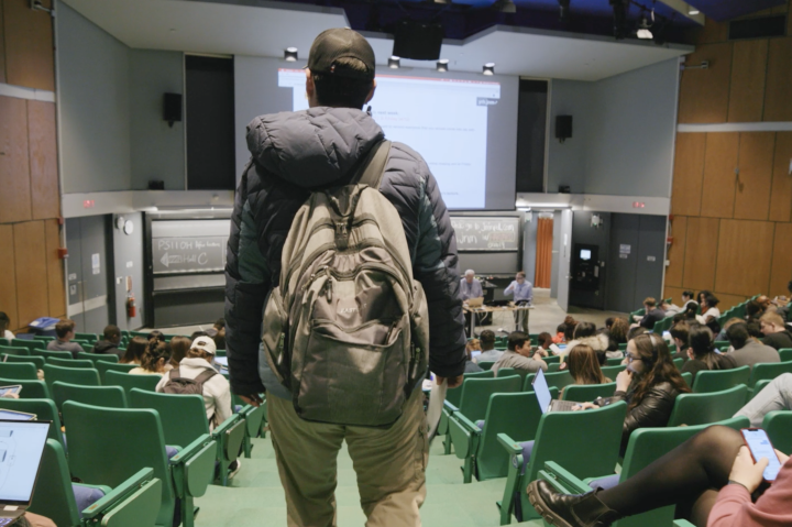 back of male student shown wearing backpack and walking into class
