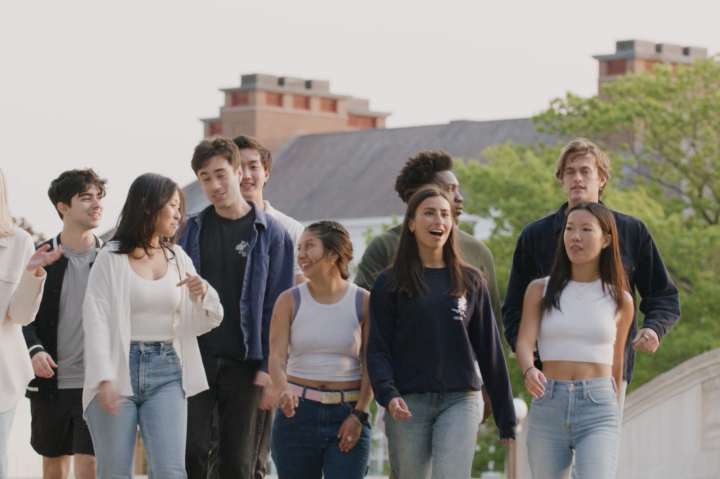 group of students laughing and talking while walking over a bridge over the Charles River