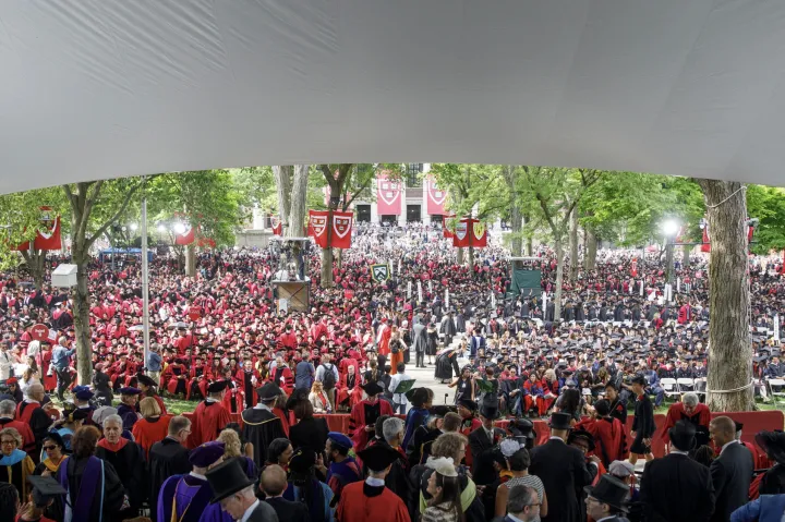 Large crowd of graduates in caps and gowns at an outdoor commencement ceremony.