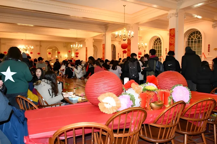 A crowded room decorated with red lanterns and festive decor, filled with people socializing around tables.