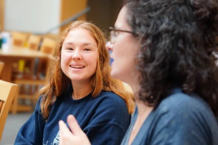 Two people sitting at a table in a dining area, engaged in conversation.