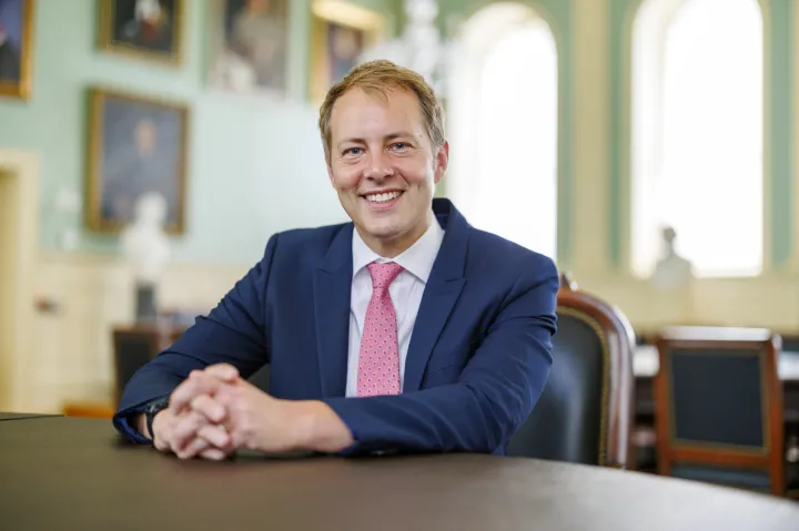 David Deming smiling while sitting at a table in a formal room.