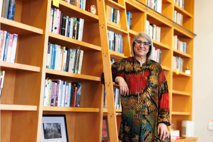 Banaji is standing and smiling in front of a large wall of books.