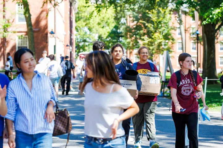 Students walk on campus, some carrying boxes and supplies, during move-in day.