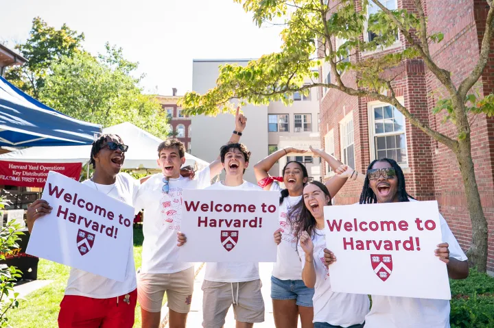 Harvard College students smile while holding "Welcome to Harvard" signs to welcome the incoming class on move-in day.