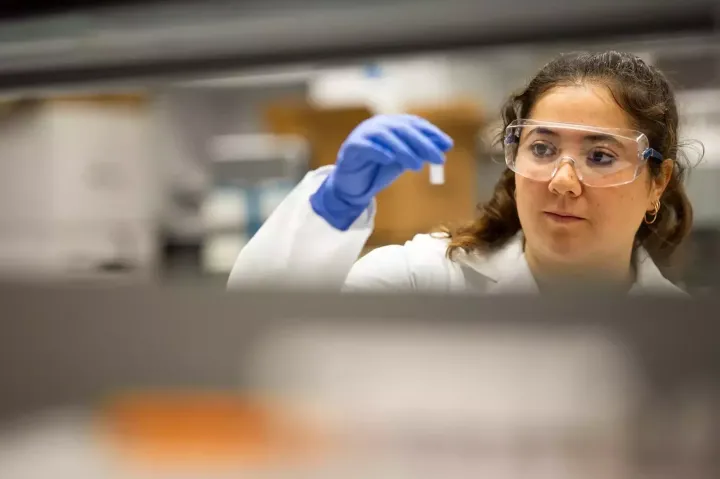 Olivia Hogan-Lopez in gloves and lab attire, looking at small test tube