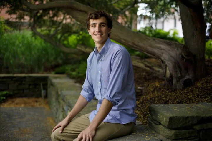 Bradford Kimball sitting on a stone bench outdoors, smiling, with a tree in the background.