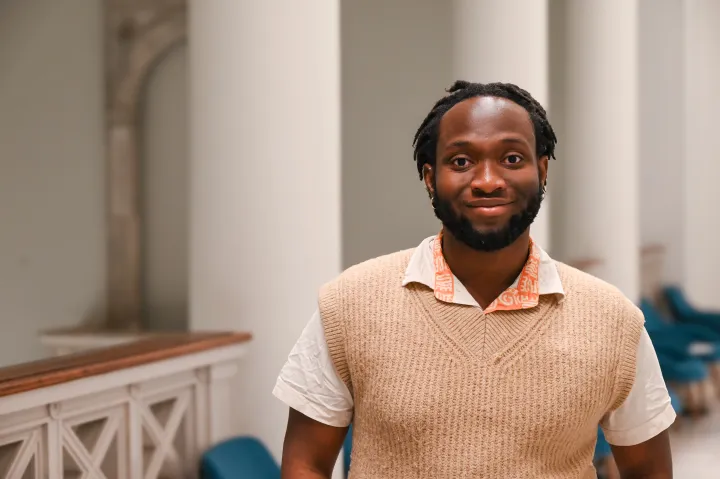 Hassan smiles while standing in a classroom hallway.