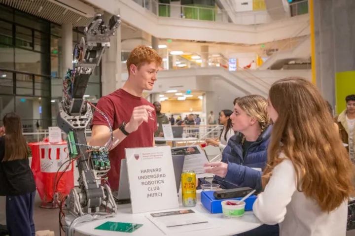 Two female students second-year students learn about the Harvard Undergraduate Robotics Club at Convocation.