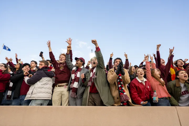 A line of Harvard College students cheer empatically in the front row at the Harvard-Yale game.