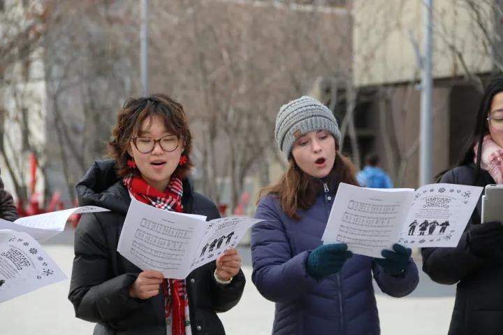 Two female students read sheet music while singing outside on the Harvard campus.