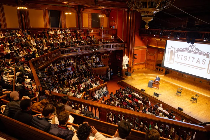 Interior of Sanders Theatre featuring two men on stage with full balconies