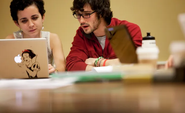 Two students sharing a laptop and speaking to one another