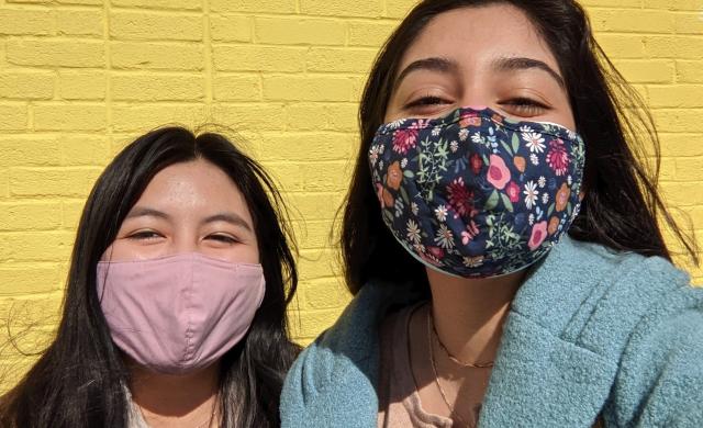 Two girls standing in front of a yellow wall.