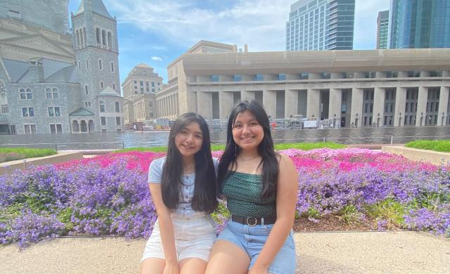 Two girls sitting by flower beds.