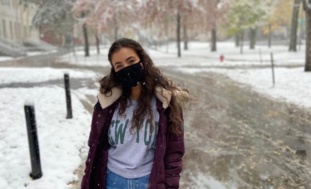 Girl in a big dark red coat in a park while it is snowing. 
