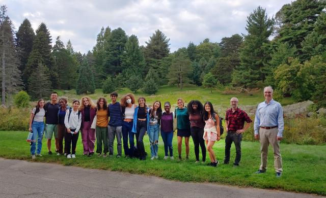 Group picture of students and professors standing beside a road with trees in the background.