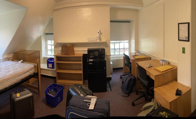 Picture of a dorm room with luggage and unorganized furniture.