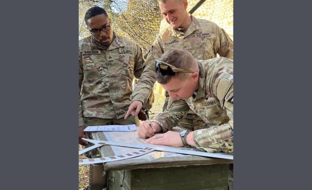 Three men look at papers on a table, including Henry Sullivan Atkins '20