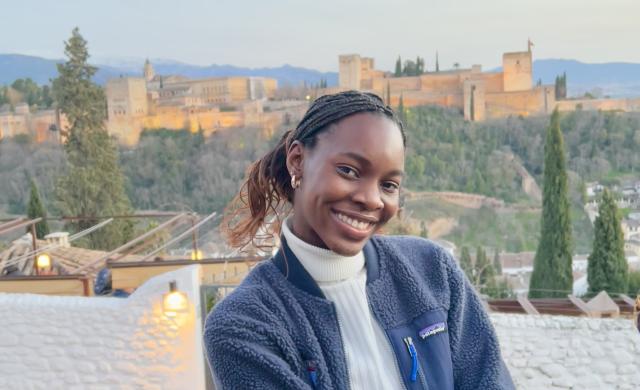Writer smiling in front of Granada's Alhambra, a castle-like structure on the horizon.