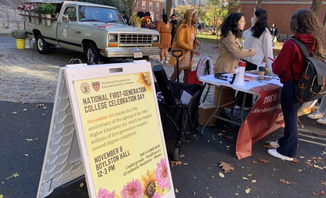 Picture of "National First-Generation College Celebration" sign with students and a truck in the background.