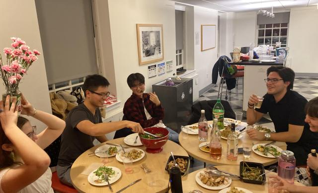 A group of friends sitting around dinner tables, some posing for the picture and some being extra silly for the picture. 