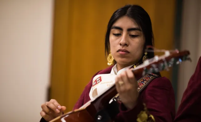 A female mariachi musician holds her instrument while wearing her mariachi suit