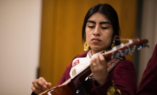 A female mariachi musician holds her instrument while wearing her mariachi suit