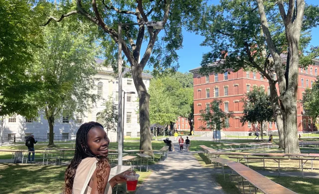 Author walking through Harvard Yard with hibiscus drink, smiling. 