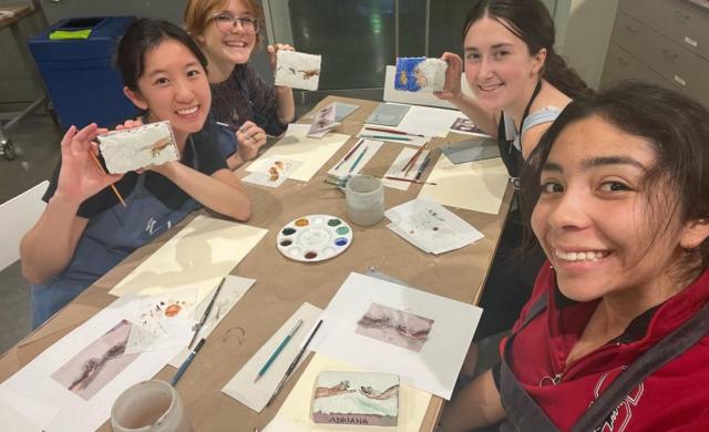 Four students smiling and surrounding a table with artworks