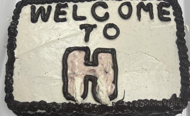 Image of a cake with white and black frosting and the words “Welcome to H” written on top.