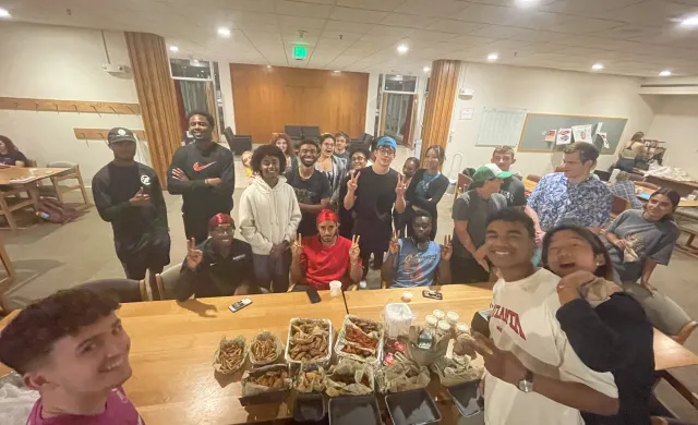 Studens gathered around a table full of food 