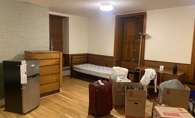 A picture of a room during move in day, with suitcases and boxes along with the furniture. The room, undecorated, looks new.