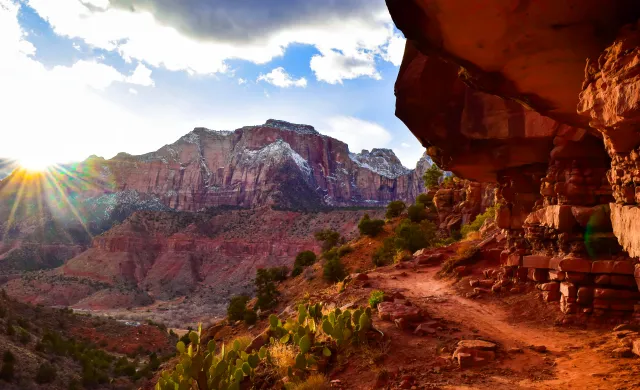 A picture of the Watchman Trail with the setting sun and snow-capped mountains in the background.