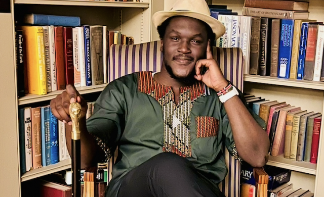 Photo of David sitting amongst some bookcases filled with books