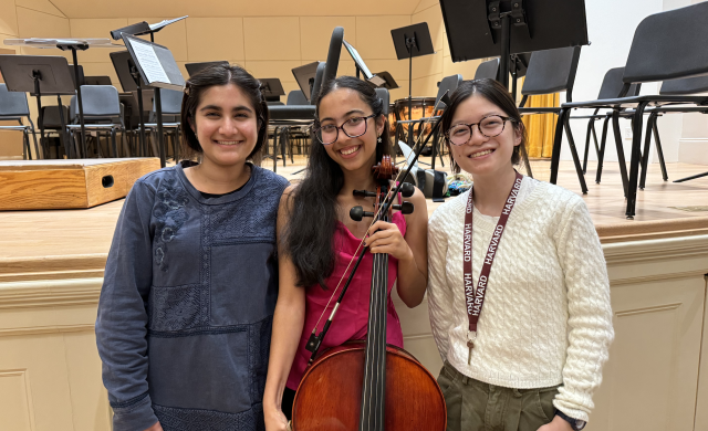 Meena holding a cello at the end of her concert, smiling and standing beside two of her roommates who came to celebrate with her.