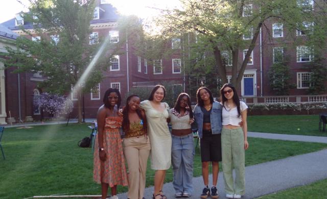 Six friends standing together and smiling in a sunny Harvard courtyard.