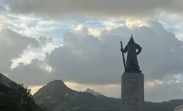 Picture of a plaza in the afternoon with a statue and people walking around