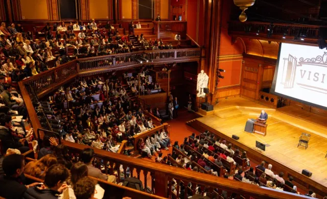 A lecture held in Sanders Theater with the word VISITAS projected onto a screen.